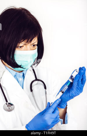 Femme médecin en blouse blanche et masque médical sur fond blanc est titulaire d'seringue à insuline et de la médecine dans une ampoule - Image Banque D'Images