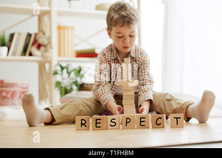 Cubes en bois avec mot respect en mains de petit garçon à la maison. Image conceptuelle sur les droits de l'enfant, l'éducation, l'enfance et des problèmes sociaux. Banque D'Images