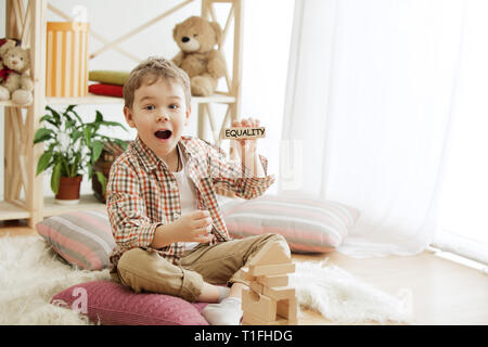 Cubes en bois avec word l'égalité dans les mains d'happy smiling little boy à la maison. Image conceptuelle sur les droits de l'enfant, l'éducation, l'enfance et des problèmes sociaux. Banque D'Images