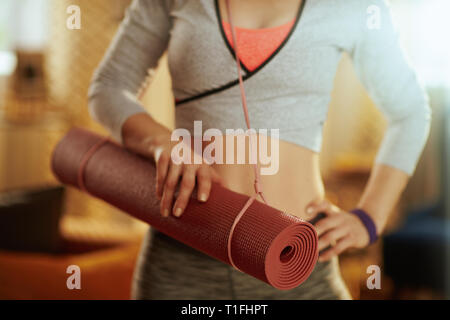 Gros plan sur le tapis de fitness dans la main de femme en bonne santé à la maison moderne. Banque D'Images