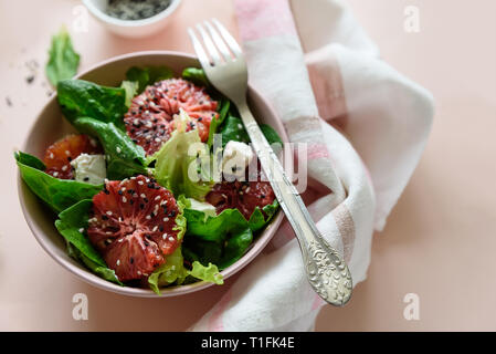 Salade fraîche de printemps avec l'orange sanguine, la laitue, les épinards et les graines de sésame sur fond rose. Vue d'en haut. Selective focus Banque D'Images