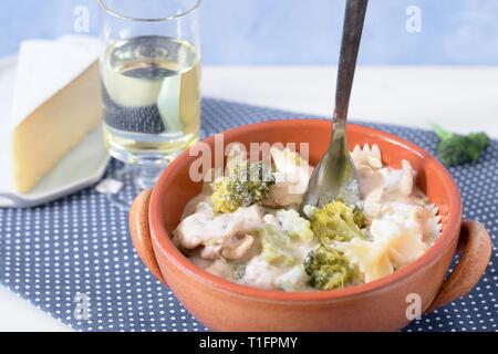 Bol de pâtes chaudes à la crème de brocoli et de la viande de poulet. Coincé dans la fourchette le repas, vin blanc en verre haut, du fromage sur la plaque, peu servi sur bleu pol Banque D'Images