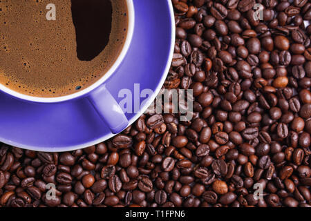 Tasse de café en violet sur la table entourée de grains de café Banque D'Images