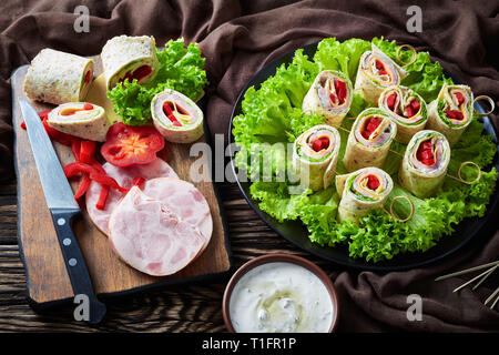 Le pain des sandwichs roulés sur une brochette dans une assiette. les ingrédients et la crème d'ail sauce dans un bol sur une table en bois rustique avec un tissu marron, Banque D'Images