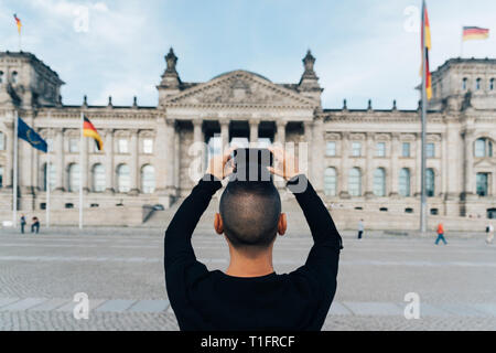 Libre d'un jeune homme de race blanche, vu de derrière, de prendre une photo de la façade du bâtiment du Reichstag à Berlin, en Allemagne, avec son smartphone Banque D'Images