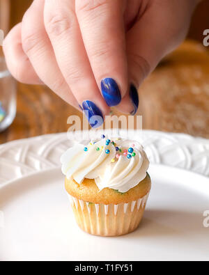 Tomber sur un sprinkles couleurs pastel givré fraîchement mini cupcake. La main seulement. Banque D'Images