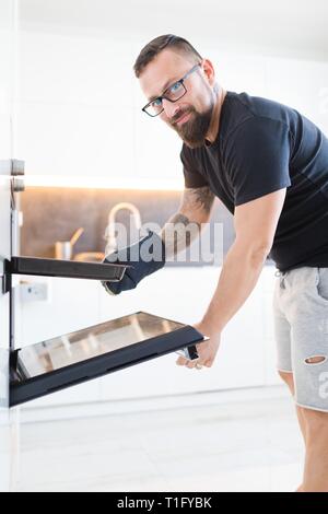Homme en noir T-shirt blanc moderne en cuisine. Tatouage sur la main droite. Banque D'Images