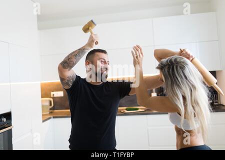 Mari et femme dans l'affrontement avec cuisine rouleau à pâtisserie et la viande maillet. Côté négatif de la relation entre l'homme et de la femme. Banque D'Images