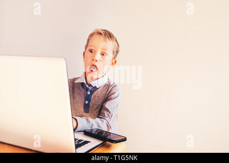 Enfant travaillant à son ordinateur portable blanc avec surprise face. Banque D'Images