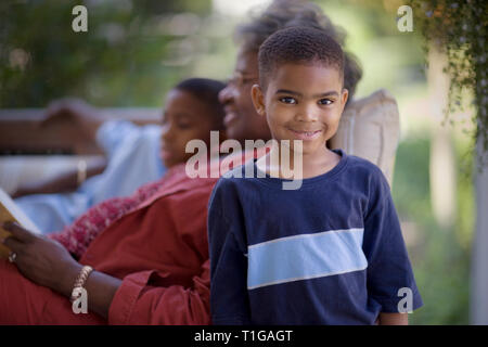 Portrait d'un jeune garçon debout à côté de sa grand-mère mature allongé sur une table de lecture avec son frère. Banque D'Images