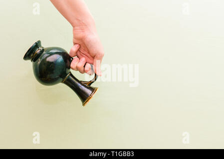 La fille main est titulaire d'un vase antique. Vase noir d'un ornement et une poignée sur un fond vert Banque D'Images