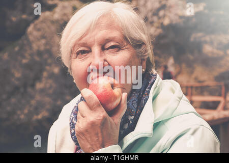 À la recherche en santé senior woman eating apple aux cheveux gris à l'extérieur dans le parc Banque D'Images