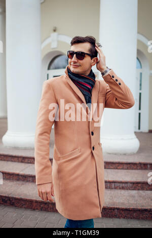 Élégant jeune homme marchant dans la ville. Beau gars portant des vêtements classiques et des accessoires. Mode de rue. Homme cheveux contrôle Banque D'Images