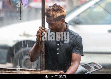 Nosy Be, Madagascar - Janvier 17th, 2019 : un homme travaillant à démonter son étal sous une pluie battante à Nosy Be, Madagascar. Banque D'Images