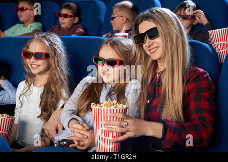 Des enfants assis dans le cinéma, le théâtre, le port de lunettes 3D, regarder la première de nouveau Film ou dessin animé. Mère et fille joyeuse holding seau de maîs éclaté, profitant de film. Banque D'Images