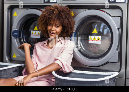 Young black African American Woman waiting ses vêtements pour être lavés dans une laverie automatique Banque D'Images