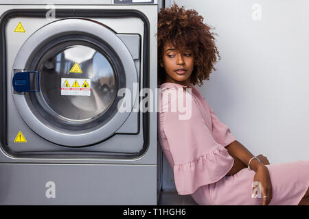 Young black African American Woman waiting ses vêtements pour être lavés dans une laverie automatique Banque D'Images