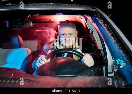 Conducteur dans une veste en cuir dans la voiture dans l'obscurité. Séance photo de nuit Banque D'Images