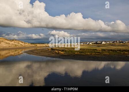 Ciel bleu et nuages reflétés dans les eaux calmes d'Afon, Crigyll avec le village au loin, conseil informatique, Anglesey, au nord du Pays de Galles, Royaume-Uni Banque D'Images