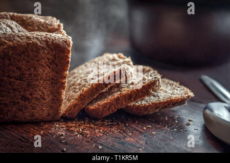 Libre de produits frais biologiques faits maison pain de grains entiers avec croûte croustillante et la vapeur chaude coupé en tranches sur une table de cuisine rustique avec des miettes Banque D'Images