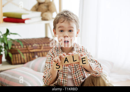 Cubes en bois avec word vente en mains de happy smiling little boy à la maison. Image conceptuelle à propos de la vente d'une maison Banque D'Images