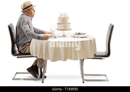 Heureux senior man blowing candles on cake une table dans un restaurant isolé sur fond blanc Banque D'Images