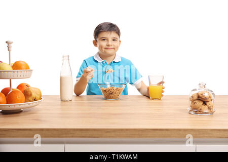 Petit écolier de manger les céréales et boire du jus d'orange à un comptoir en bois isolé sur fond blanc Banque D'Images