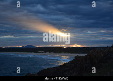 La lumière du soleil brille à travers les nuages de tempête coucher de soleil surplombant l'océan Pacifique, Australie, de la veille de la super lune, les rayons reflétés dans la mer Banque D'Images