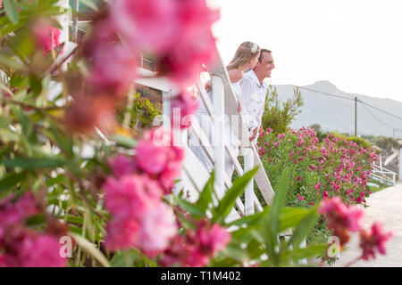 Vue romantique du couple dans des vêtements blancs sur un balcon avec des fleurs de bougainvillées rose autour. Magnifique paysage de montagne au-dessus de soleil au coucher du soleil. Banque D'Images