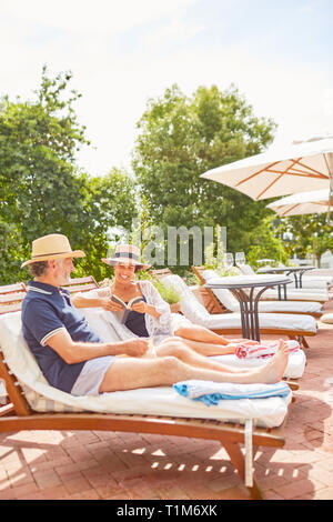 D'âge mûr se reposer, lire sur les chaises longues au bord de la piscine ensoleillée resort Banque D'Images