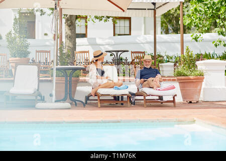 Young couple relaxing on lounge chairs at poolside resort Banque D'Images