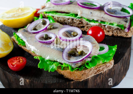 Filet de hareng avec sel, poivre, herbes, l'oignon et de citron sur la plaque noire sur fond blanc. Vue de dessus de la nourriture saine. Banque D'Images