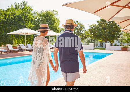 Young couple holding hands, marcher le long de sunny resort piscine Banque D'Images