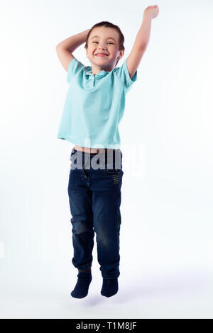 Little smiling boy aux cheveux noirs en jeans, T-shirt polo bleu saute et s'amuser sur un fond blanc dans un studio photo Banque D'Images