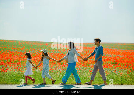 Famille enceinte tenant les mains, marchant le long du champ de pavot rouge rural ensoleillé Banque D'Images