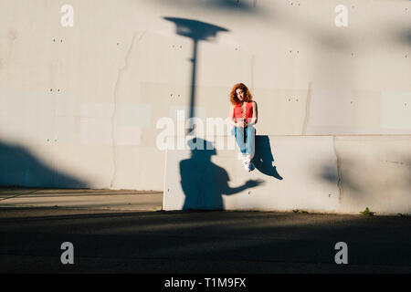 Ombre regardant une jeune femme utilisant un smartphone sur un mur urbain Banque D'Images
