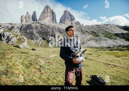 Garçon avec tablette numérique et joystick contrôlant drone dans le parc naturel ensoleillé de Drei Zinnen, Tyrol du Sud Banque D'Images