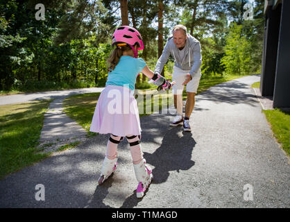 L'enseignement du père à sa fille d'sur patins à roulettes. Happy kid casque en patinage artistique. d'apprentissage Famille de passer du temps ensemble. Journée ensoleillée sur subur Banque D'Images