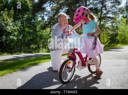 L'enseignement du père sa fille à circuler à bicyclette. Happy kid learning riding bike. Famille de passer du temps ensemble. Journée ensoleillée sur suburb street. Banque D'Images