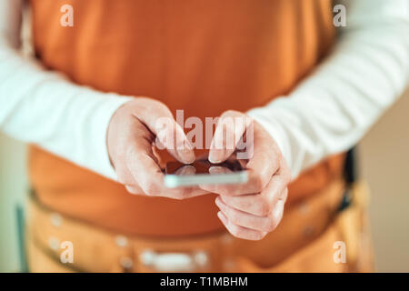 Female carpenter est l'utilisation de téléphone mobile pour la messagerie texte, la saisie de sms sur l'écran tactile du smartphone, selective focus Banque D'Images