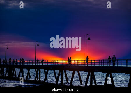 La plage de Glenelg jetty avec silhouettes de personnes au coucher du soleil d'hiver, l'Australie du Sud Banque D'Images