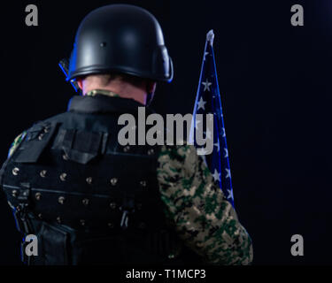 Soldat en treillis de l'armée d'un fusil d'assaut et holding US flag, tourné à partir de l'arrière Banque D'Images