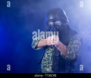 Soldat en treillis de l'armée portant le masque à gaz fusil d'assaut holding dans la brume sèche de fumée bleue Banque D'Images