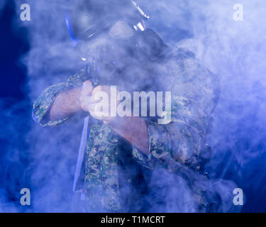 Soldat en treillis de l'armée portant le masque à gaz fusil d'assaut holding dans la brume sèche de fumée bleue Banque D'Images