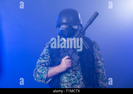 Soldat en treillis de l'armée portant le masque à gaz fusil d'assaut holding dans la brume sèche de fumée bleue Banque D'Images