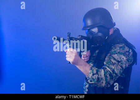 Soldat en treillis de l'armée portant le masque à gaz fusil d'assaut holding dans la brume sèche de fumée bleue Banque D'Images