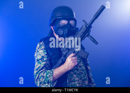 Soldat en treillis de l'armée portant le masque à gaz fusil d'assaut holding dans la brume sèche de fumée bleue Banque D'Images