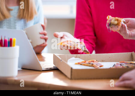 Happy woman Eating Pizza et au pouvoir. Trois jeunes collègues joyeux en train de déjeuner ensemble au travail. Équipe de création autour de Banque D'Images