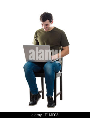 Cheerful young man working on laptop assis sur une chaise isolée sur fond blanc. Creative freelancer guy travailler de la maison à son carnet compu Banque D'Images