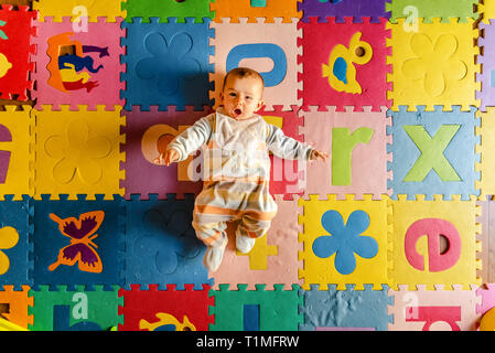 Adorable smiling baby vu de dessus en pyjama, couché sur le dos dans son jouet prix. Banque D'Images